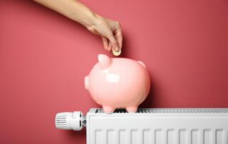 Ein Sparschwein steht auf einem Heizkörper und wird von einer Hand mit geld gefüllt.