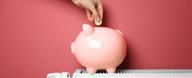 Ein Sparschwein steht auf einem Heizkörper und wird von einer Hand mit geld gefüllt.