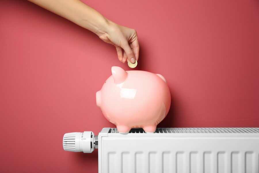 Ein Sparschwein steht auf einem Heizkörper und wird von einer Hand mit geld gefüllt.