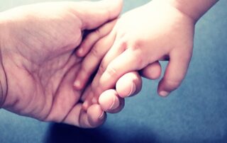 Eine Erwachsenenhand hält die Hand eines Kindes.