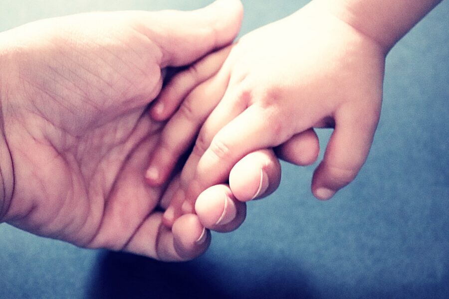 Eine Erwachsenenhand hält die Hand eines Kindes.